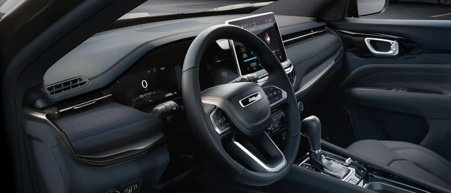 2026 Jeep Compass interior front cabin view showing the steering wheel, dashboard, infotainment screen, and front seats.